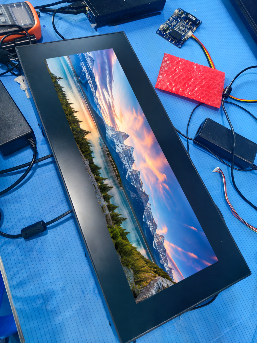 Ultra-tall bar-type LCD display on a workbench showing a mountain landscape image