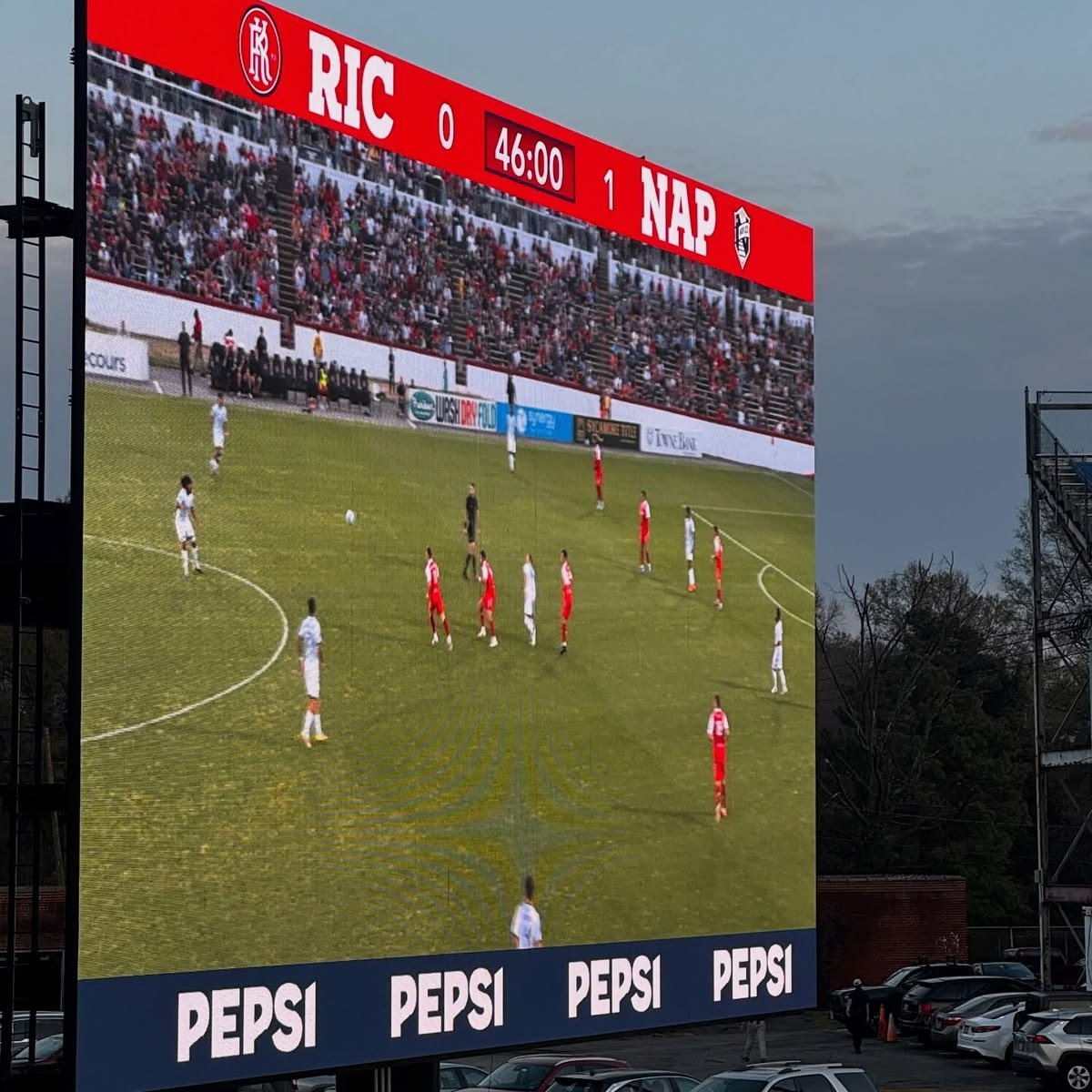 Large outdoor LED stadium scoreboard showing a soccer match