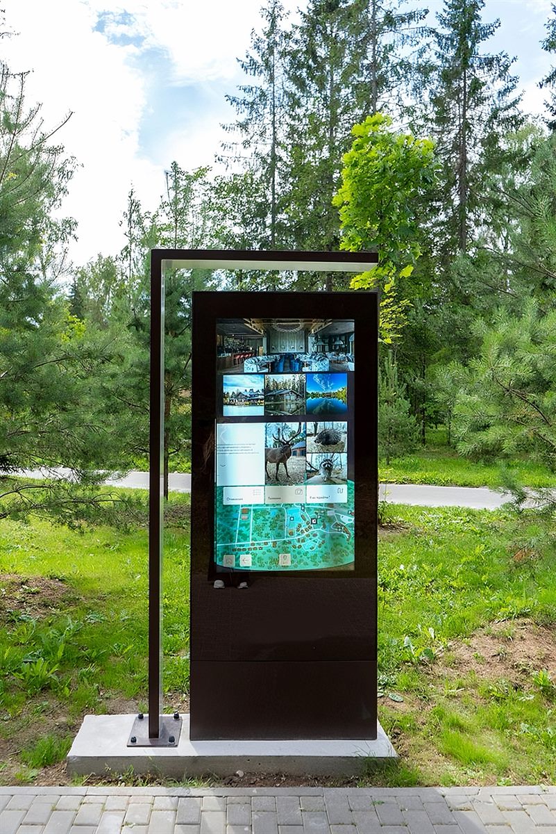 Outdoor digital wayfinding totem in a forest park showing maps and photo content