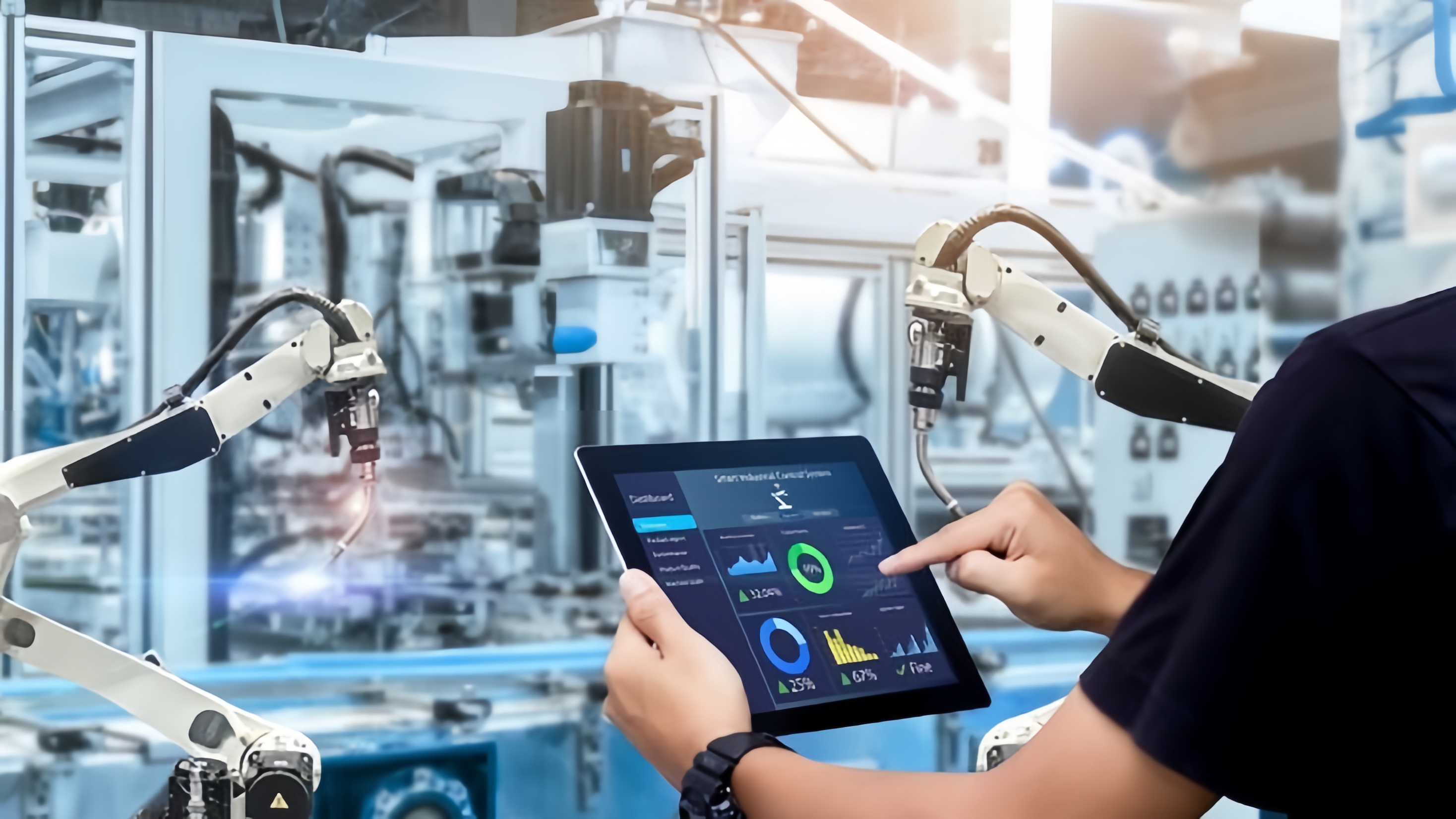 Operator using a tablet-based smart industrial control system on a factory floor with robotic arms